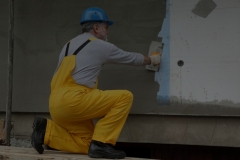 Worker spreading mortar over styrofoam insulation and mesh with trowel